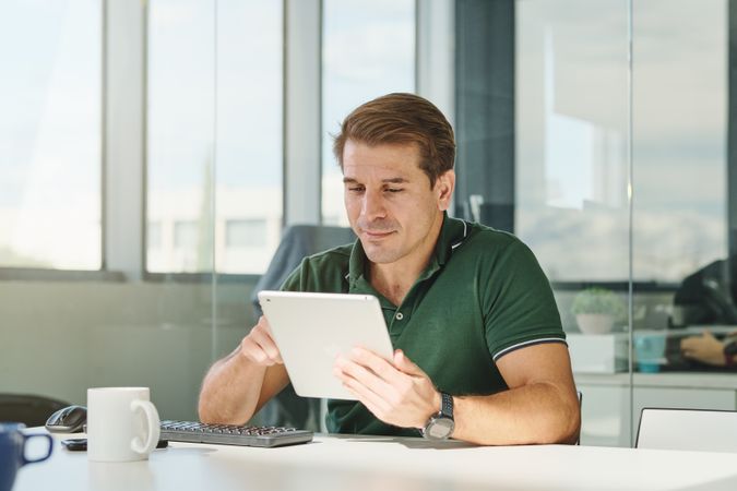 Positive businessman typing on tablet in office
