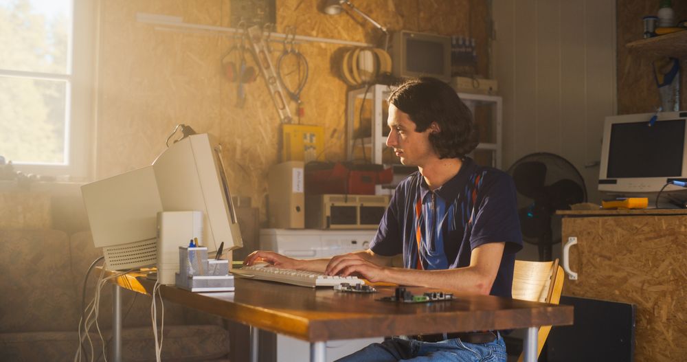 White Male Computer Engineer Coding On Old Desktop PC And Inspecting Microchip In Retro Garage.