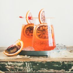 Two glasses of an orange cocktail with blood orange slices, and cocktail picks, close up