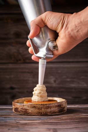 Crop person decorating cake with whipped cream