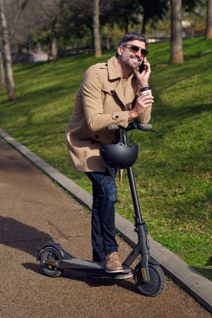 Content man talking on smartphone on scooter