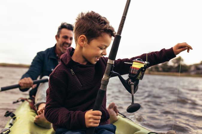 Young child holding fishing line and pole sitting in kayak with father