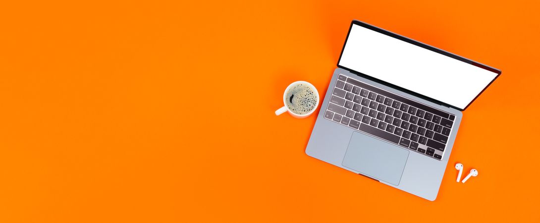 Banner of laptop on orange desk with mug of cup of coffee or tea, and earbuds with copy space
