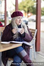 Woman holding a cup while sitting at an outdoor cafe 0LYaR5