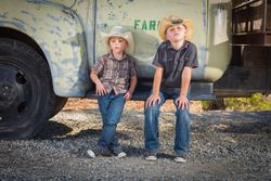 Two Boys Wearing Cowboy Hats Leaning Against an Antique Truck in a Country Setting