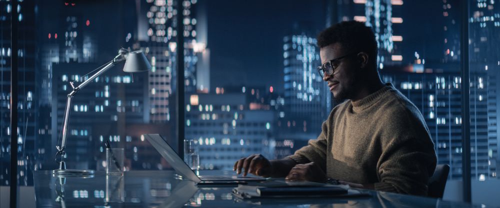 Successful Black Businessman Working on Laptop Computer in Big City Office in the Evening.
