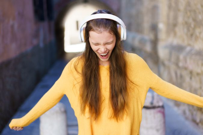 A Joyful Young Woman is Delightedly Enjoying Music While Wearing a Bright Yellow Sweater