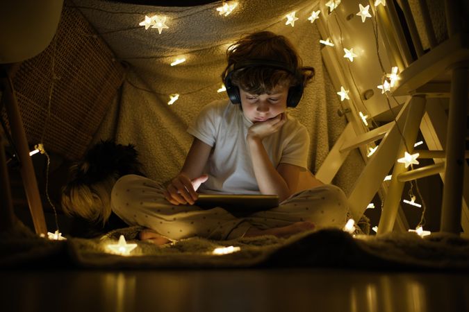 Bored boy watching film on tablet in tent