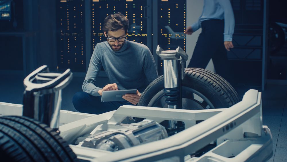 Automobile Design Engineer Sitting Beside Hybrid Electric Car Chassis Platform Prototype, Using Tablet Computer for Design Enhancement