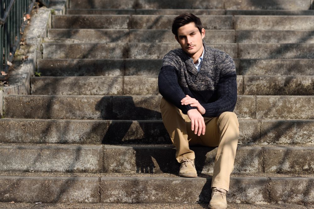 Man in woolen sweater sitting on steps outside with shadows of trees
