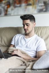 Man relaxing on sofa using laptop at home 0KMBl1