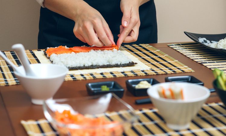 Hands of chef placing salmon in sushi roll on mat