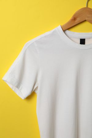 Hanger with blank t-shirt on yellow background, space for text