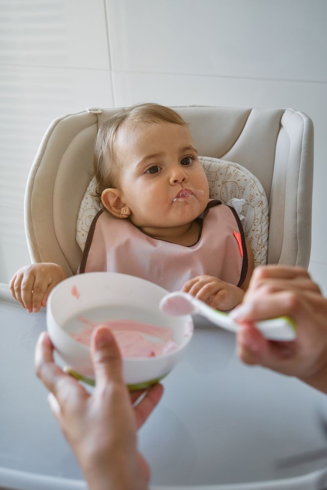 Crop person feeding daughter with spoon
