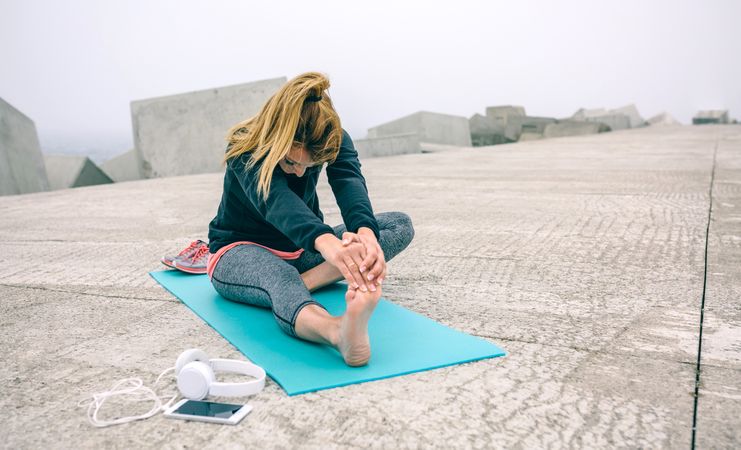 Young woman stretching legs by sea pier