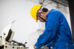 Male in blue jumpsuit and PPE gear operating machinery in manufacturing plant