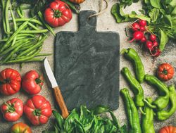 Fresh vegetables arranged with dark cutting board and knife in center