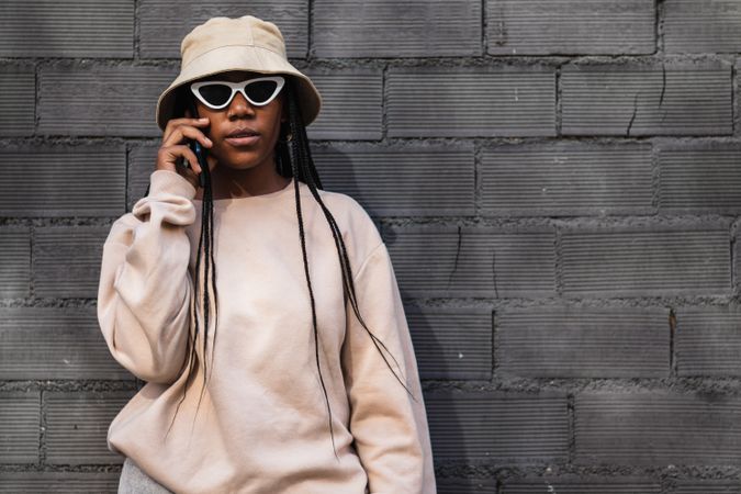 Black woman talking on smartphone near brick wall