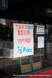 Handmade sign on restaurant window offering 1/2 price alcohol takeout 4d8va4