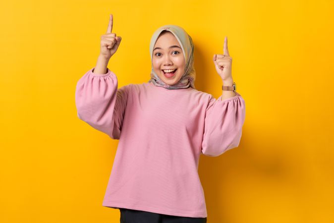 Happy Muslim woman on the phone and pointing two fingers upwards holding smart phone