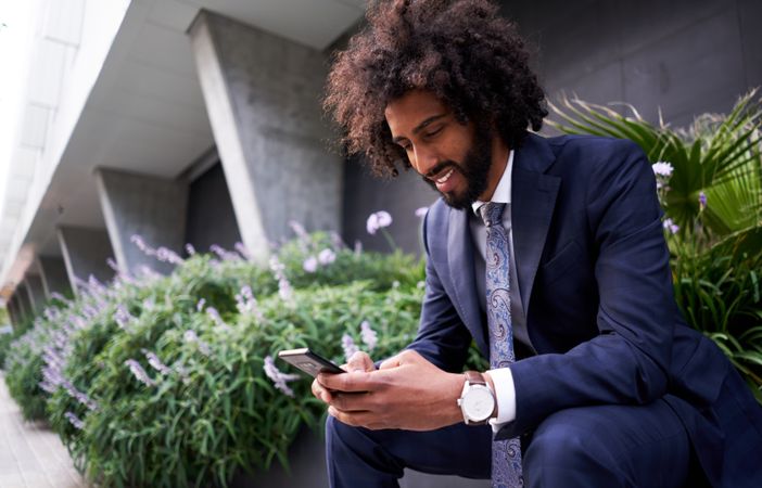 Joyful man in suit sitting outside and messaging
