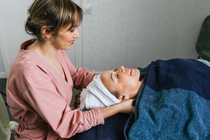 Smiling masseuse doing massage for woman in spa salon