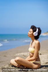 Woman in yellow swimwear sitting and meditating on beach looking out to the ocean, vertical 4OQ8j0