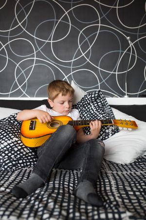 Young blonde boy playing toy guitar