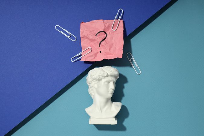 Marble bust of David with crumpled pink post it note with question mark and paper clips on blue