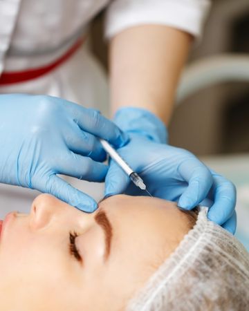 Cosmetologist at med spa injecting botox into wrinkles in female client