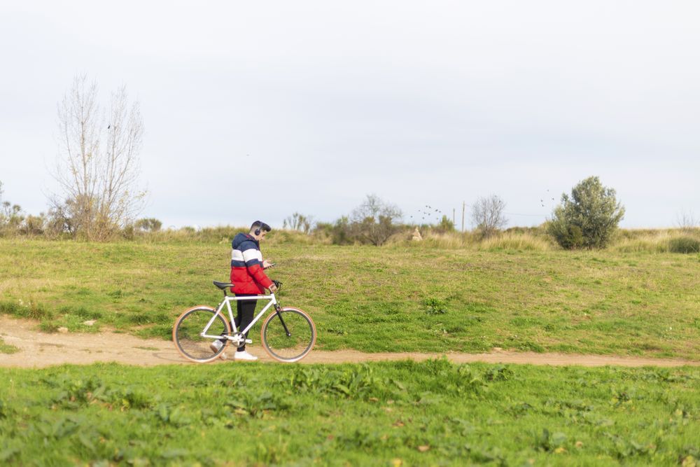 Man walking with bicycle and using a smartphone in park
