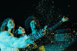 Group of female friends lit in green blue light at night throwing confetti together
