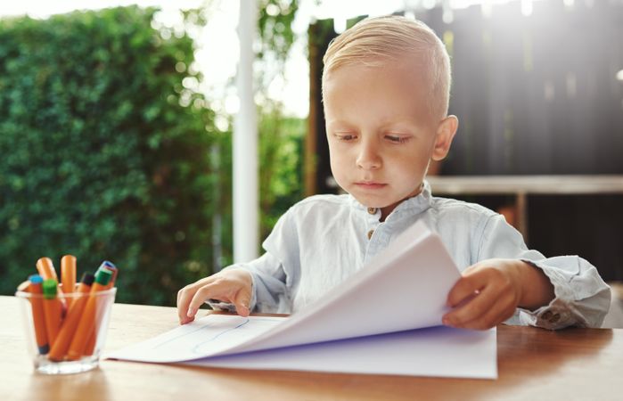 Serious blond boy drawing outside on deck