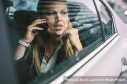 Young businesswoman sitting on back seat of a car and talking on phone 568LLb