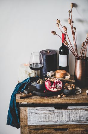 Rustic setting of wine, cheese, candle, with pomegranate, and dried poppies