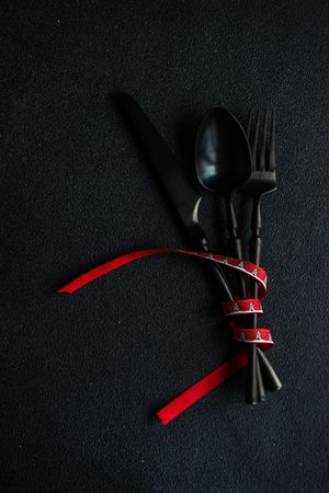 Dark knife and fork on dark background tied with festive red ribbon