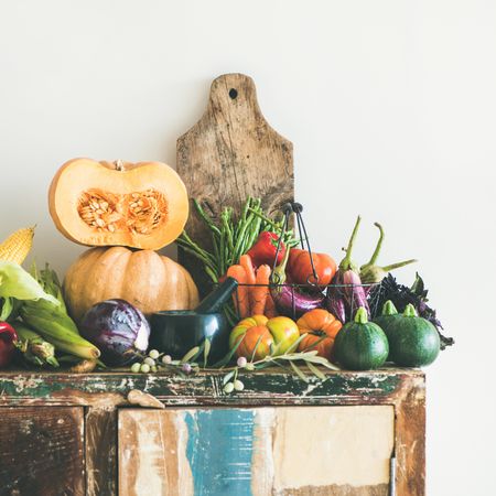 Fresh autumnal produce on kitchen counter, with halved squash and wooden board, square crop