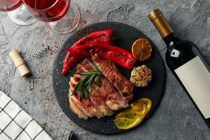 Chopped fried pork steak, vegetables and wine on gray background. Grilled food