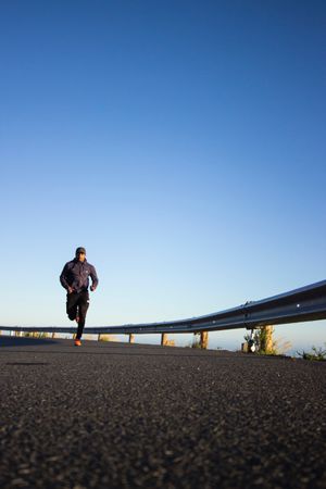 Man in jacket jogging on asphalt road under blue sky