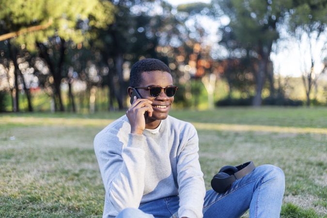 Smiling Black male with sunglasses sitting in park talking on his phone