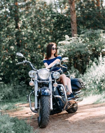 Woman sitting on cruiser motorcycle parked on dirt road