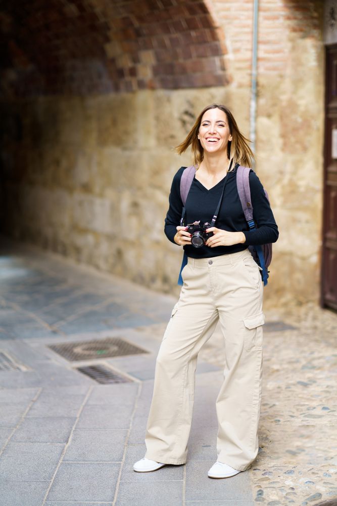 Smiling woman with camera near arched passage in old town