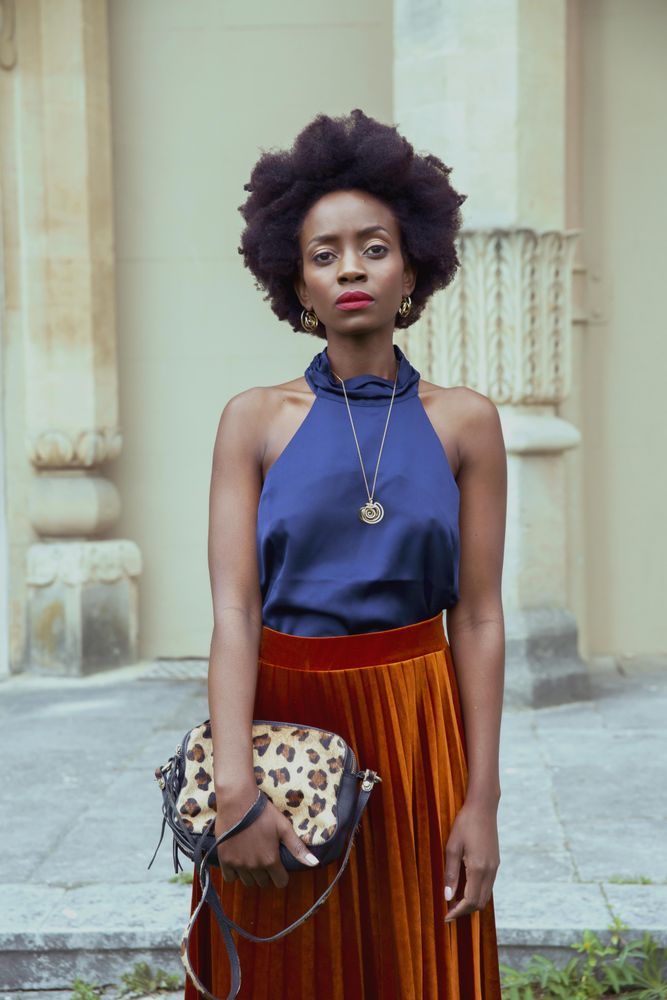 Woman in blue tank top and brown skirt standing beside building outdoor