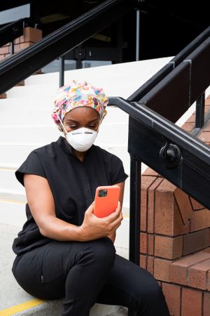 Nurse in PPE takes break outside medical building video chatting on smart phone