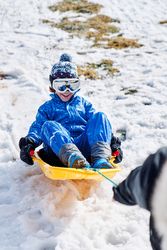 Crop parent pulling sleigh with glad son