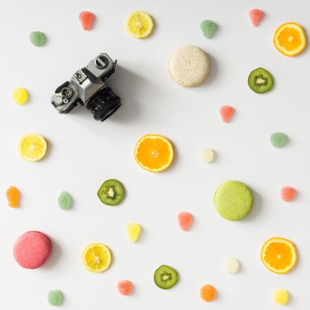 Fruit slices, gummies, and macarons and camera on light background