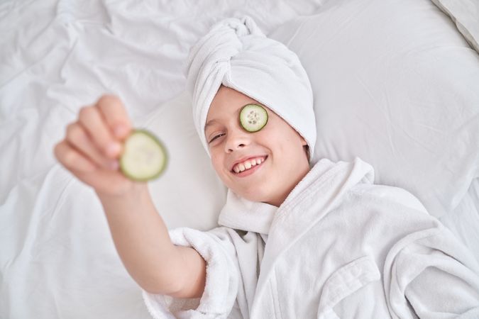 Boy with cucumber slice on eye in bedroom