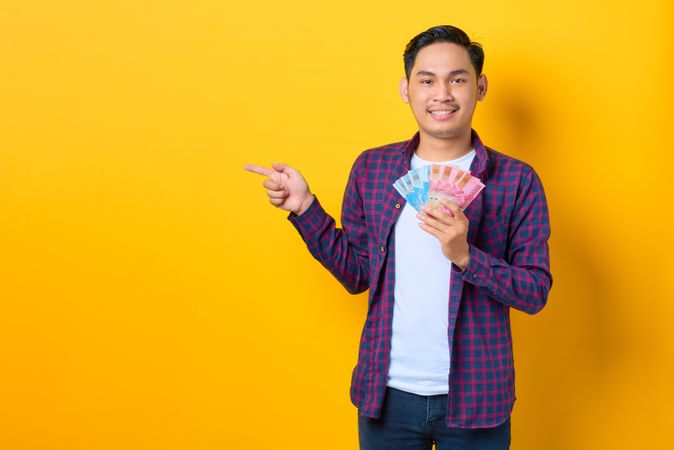 Smiling young Asian man in plaid shirt holding banknotes