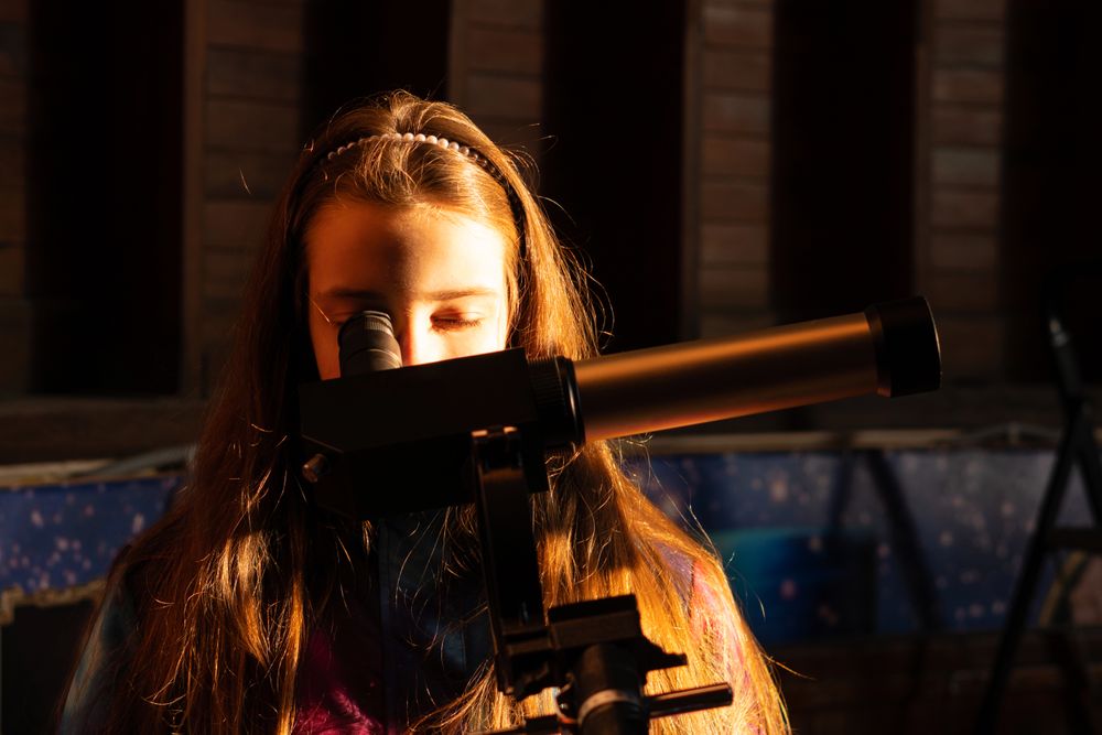 Girl with long hair studies sky through solar telescope.