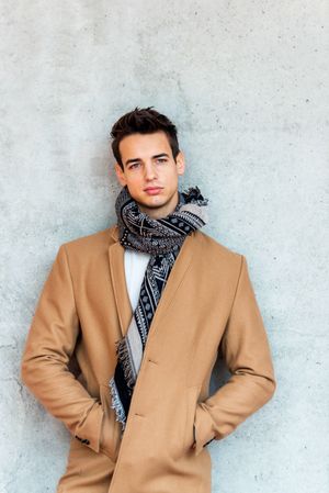 Bemused man wearing camel coat and scarf looking in distance against cement wall
